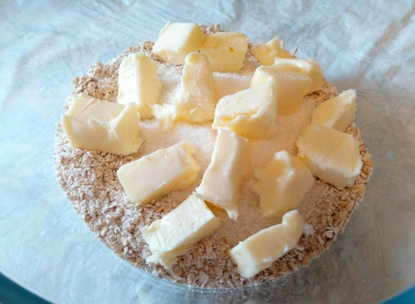 1. Этап. Геркулесовые пирожные: Добавьте к перемолотым хлопьям сахарный песок и масло, нарезанное кубиками.