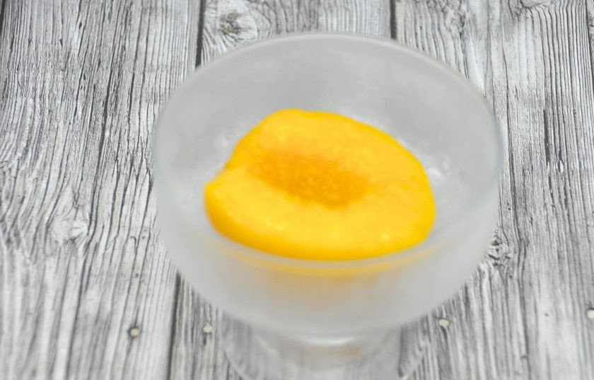 1. Этап. Персик Мельба: Все продукты для приготовления десерта должны быть очень холодными, даже креманки лучше подержать в морозилке. Достаньте креманку из морозилки, выложите персик ямкой от косточки вверх.