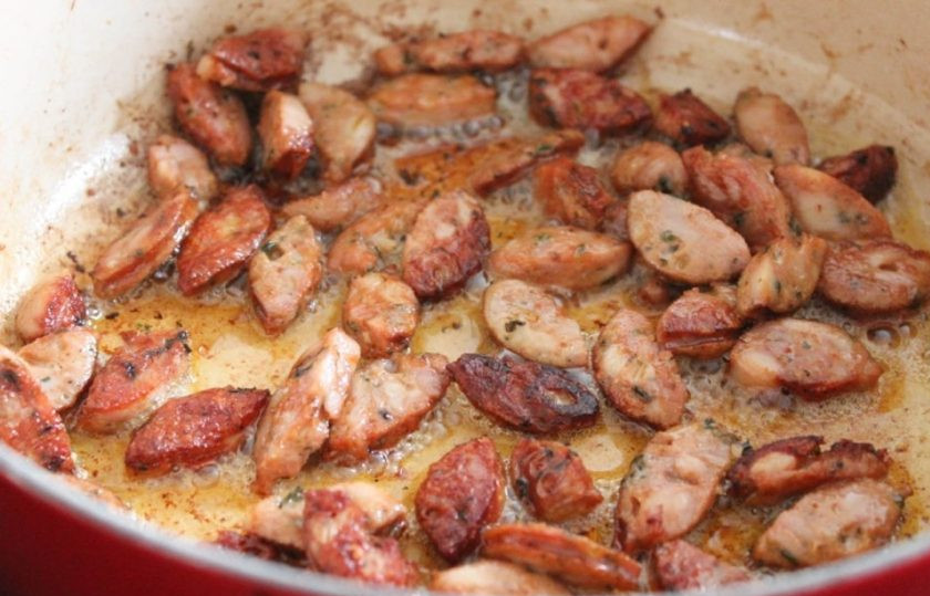 1. Этап. Овощное рагу с колбасой: Разогрейте масло в глубокой сковороде или сотейнике. Колбасу нарежьте и обжарьте в масле в течение 4-5 минут, переворачивая.