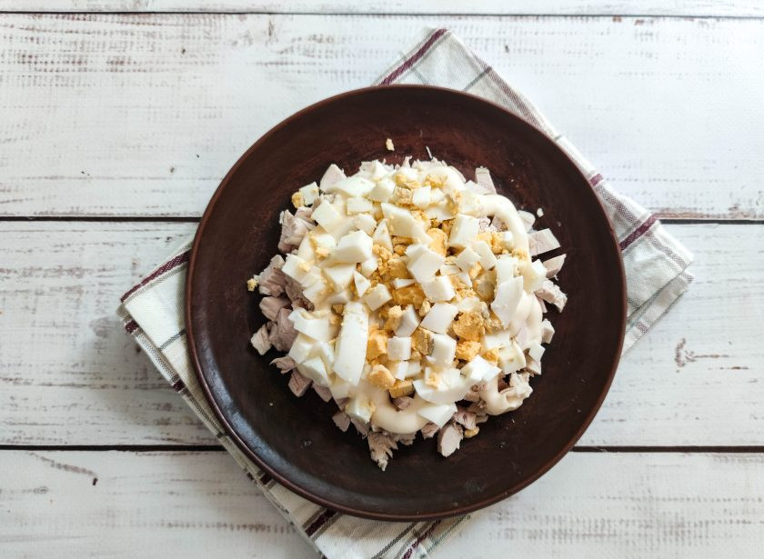 1. Этап. Салат Броненосец: Сварите яйца и опустите их в ледяную воду. Очистите яйца от скорлупы, нарежьте, выложите поверх курицы и смажьте майонезом.