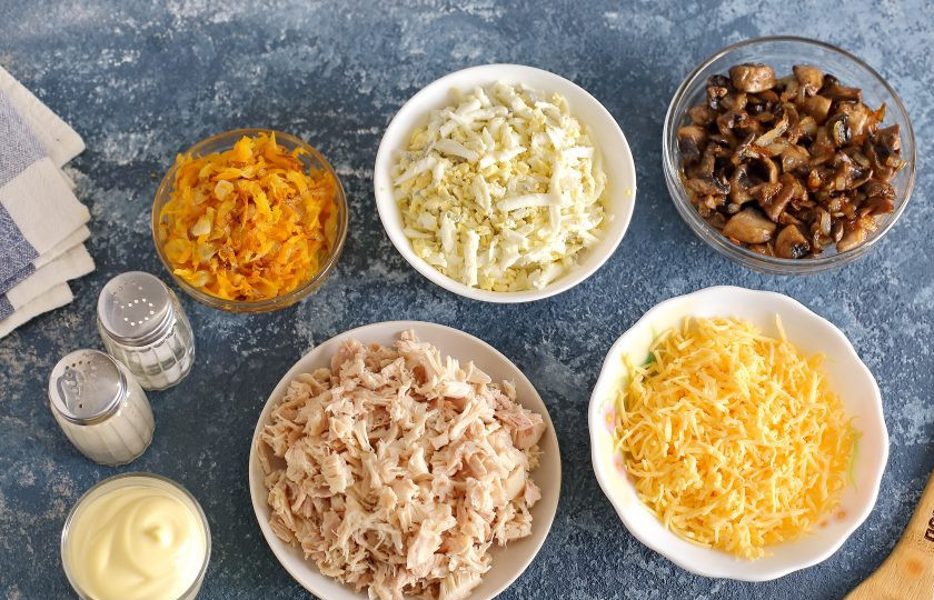 1. Этап. Слоеный салат с окорочком: Одну луковицу и морковь обжарьте до мягкости. Отдельно обжарьте нарезанную кубиками вторую луковицу с шампиньонами. Яйца натрите на крупной терке. Окорочок разделайте и нарежьте мясо небольшими кусочками. Сыр натрите на мелкой терке.