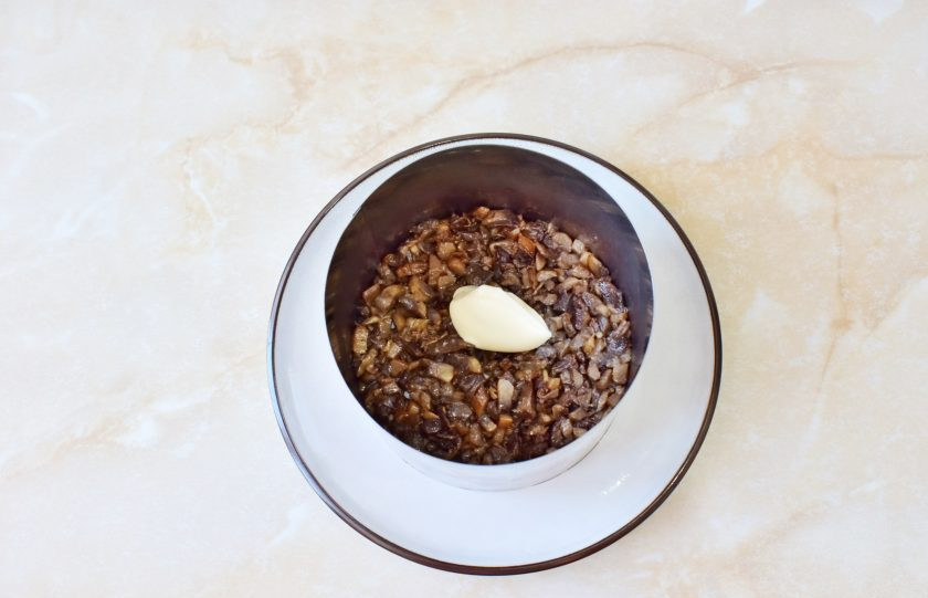 1. Этап. Салат Восторг с корейской морковью: Салат будем собирать слоями. Для этого поставьте сервировочное кольцо на тарелку и первым слоем выложите обжаренные грибы. Немного смажьте их майонезом.