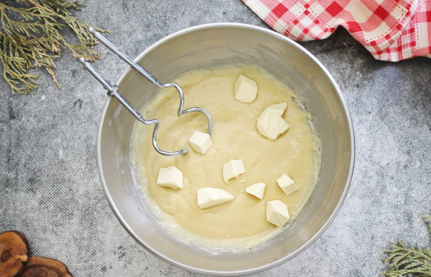 1. Этап. Очень мягкий пасхальный кулич: Холодное, но мягкое сливочное масло порежьте на мелкие кусочки и, продолжая взбивать тесто, частями добавляйте его в миску. Вымешивайте тесто в течение 8-10 минут.