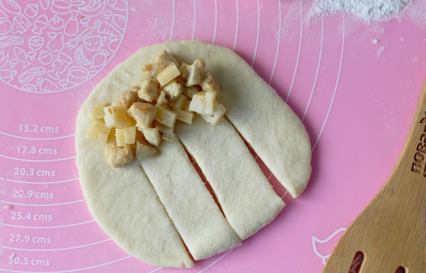 1. Этап. Булочки с курицей и сыром: Затем раскатайте каждую заготовку в форме овала и ближе к одному краю выложите начинку. Со второй стороны нарежьте тесто на 4 полоски как на фото.