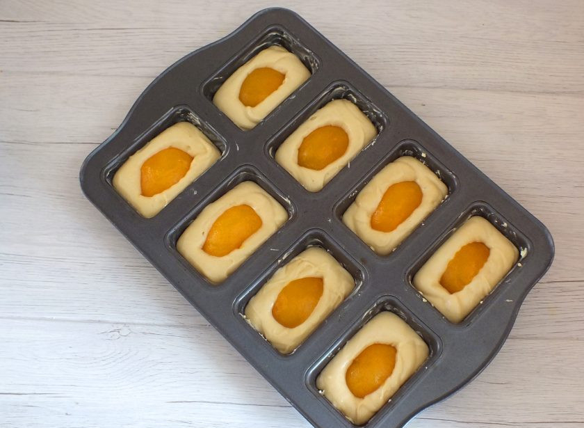 1. Этап. Кексы с персиками: Формочки для кексов смажьте обильно сливочным маслом. Разлейте тесто на 2/3 объема формочки. В серединку выложите персики и слегка 