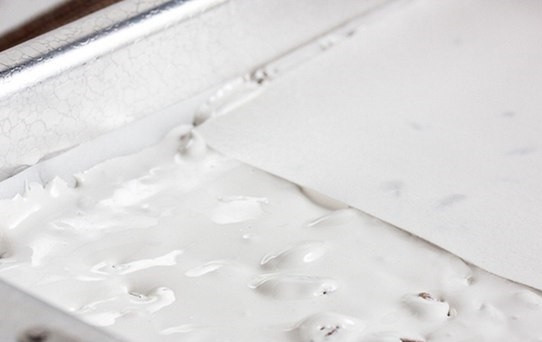 1. Этап. Нуга с миндалем: 4. На максимальной скорости взбивайте около минуты, затем тонкой струйкой влейте кипящий сироп и продолжайте взбивать. Аккуратно добавьте орехи и перемешайте. Вот и весь вариант, как сделать нугу с миндалем. Теперь переложите массу на пергамент и разровняйте.