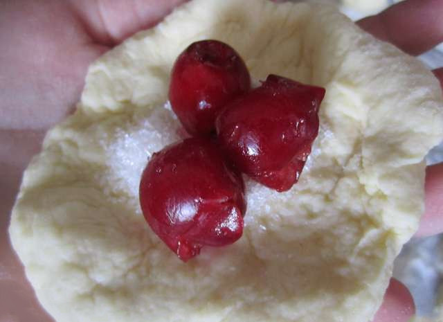 1. Этап. Пончики с вишней: Разделяем тесто на кружочки, раскатываем каждый, заворачиваем в него начинку (по половине чайной ложки сахара и немного ягод). Края защипываем хорошенько.