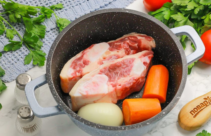 1. Этап. Холодец на костях: Выложите косточки в казан или кастрюлю, добавьте туда же овощи. Можно разрезать морковь и лук пополам.