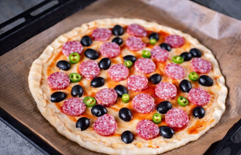 1. Этап. Мексиканская острая пицца: Поверх разложите кружочки салями, половинки маслин и колечки перчика чили.