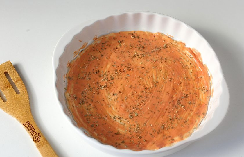 1. Этап. Пицца с тушенкой: Разделите тесто на две части. Одну часть я буду использовать для приготовления пиццы, а вторую я обычно замораживаю. Можно конечно приготовить и две пиццы одновременно. Начинка может быть одна, а можно сделать разные пиццы по содержанию. Тесто раскатайте по размеру формы, у меня 27 см. в диаметре, смажьте соусом и посыпьте специями. Я использую орегано и базилик.