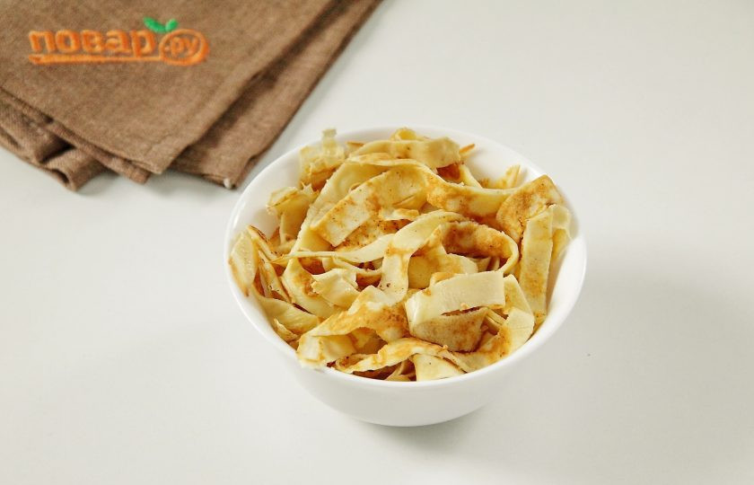 1. Этап. Слоеный салат Новогодний: На смазанной маслом сковороде испеките два блина, дайте им немного остыть и нарежьте полосками.