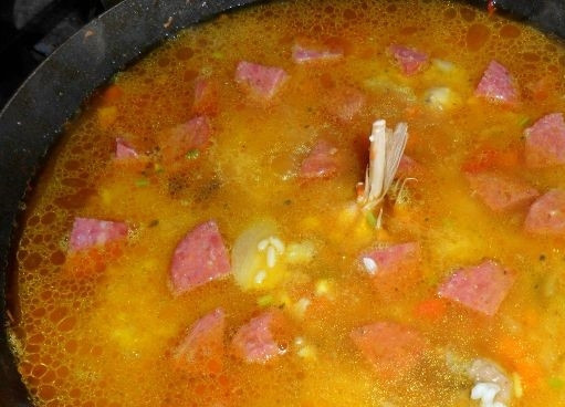 1. Этап. Испанская паэлья с курицей: 3. К ингредиентам на сковородке добавьте порезанную кусочками колбасу. Залейте горячим бульоном, приправленным куркумой. Накройте крышкой, обернув ее полотенцем. Томите блюдо на слабом огне не более 20 минут.