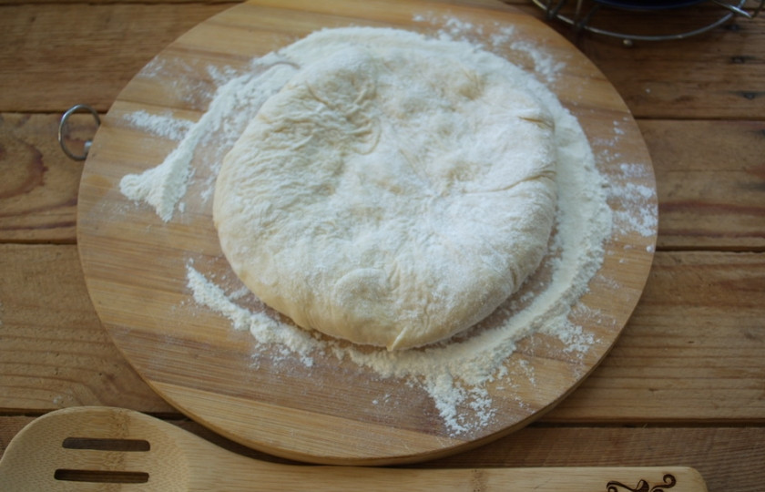 1. Этап. Осетинский пирог Царский: Разделите тесто на 3 части. Доску присыпьте мукой. 1/3 часть теста выложите на доску, разомните руками от центра к краю.