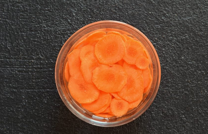 1. Этап. Розы из моркови: Морковь очистите от кожуры и нарежьте на тонкие кружочки. Замочите морковь в воде с солью на 30 минут, чтобы кружочки стали эластичными и мягкими.