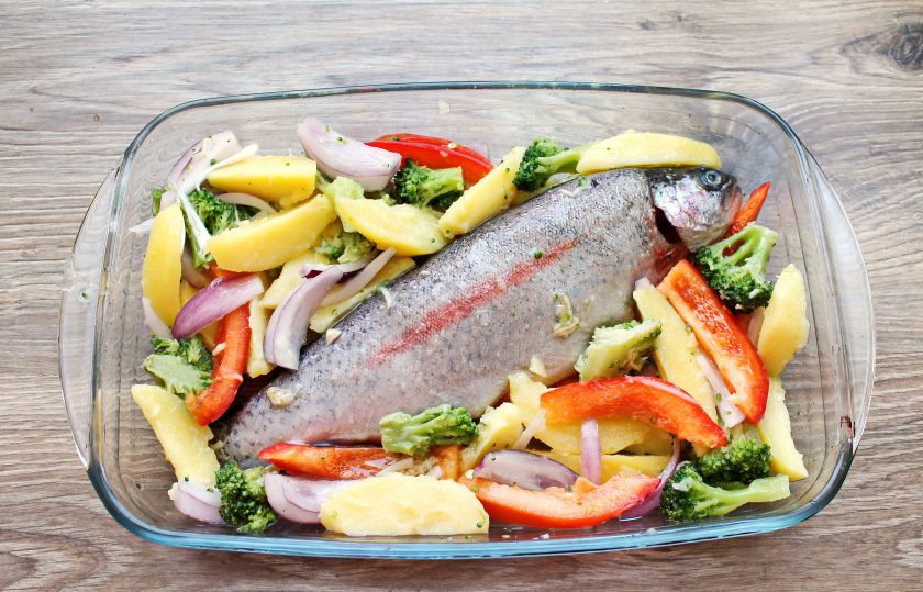 1. Этап. Радужная форель в духовке с овощами: Форму для запекания смажьте растительным маслом и выложите радужную форель. Вокруг рыбы разложите подготовленные овощи.
