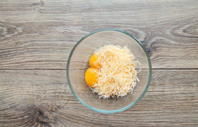 1. Этап. Судак в сырном суфле: Яйца разделите на белки и желтки. Желтки выложите в миску и добавьте сыр, тертый на средней терке.