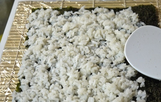 1. Этап. Роллы овощные: 5. Бамбуковый коврик оберните пищевой пленкой. Выложите на лист нори рис, чуть оставив свободным край, и распределите ровным слоем.