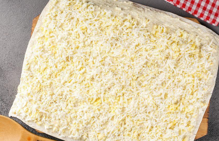 1. Этап. Рулет из лаваша с крабовыми палочками: Сверху выложите тёртые на крупной тёрке яйца и тёртый мелко плавленый сыр. Сыр по желанию можно взять любой на ваш вкус или использовать 2-3 вида одновременно. По желанию посолите и поперчите начинку по вкусу.