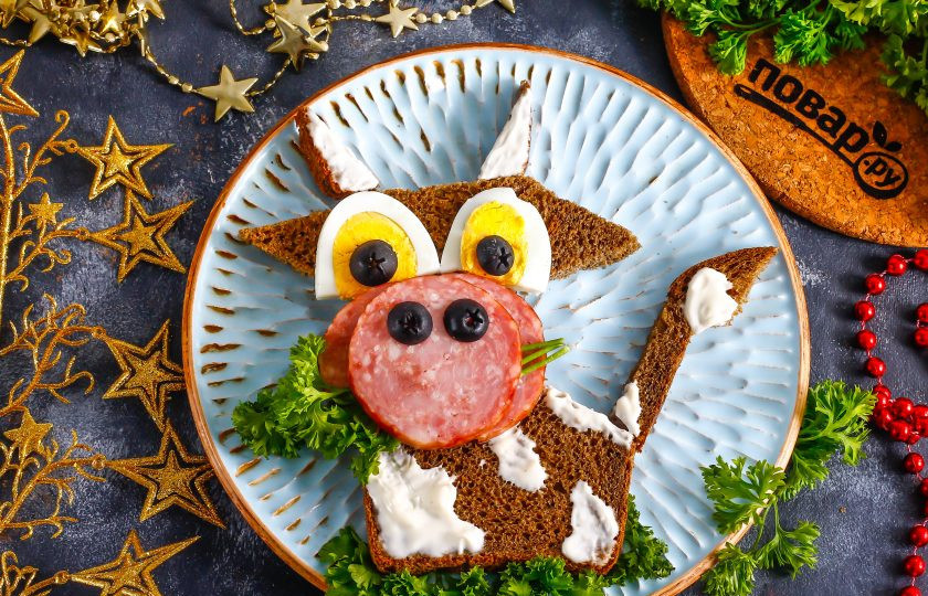 1. Этап. Бутерброд Веселый Бычок: Под первый ломтик колбасы вставьте стебельки зелени, как будто бычок их жует. Украсьте основание бутерброда свежей зеленью. Закуска полностью готова к подаче!