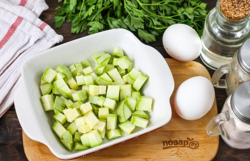 1. Этап. Овощная запеканка в микроволновке: Кабачок промойте в воде, срежьте хвостики и нарежьте овощ кубиками. Смажьте форму для запекания растительным маслом и выложите в нее кабачковую нарезку.