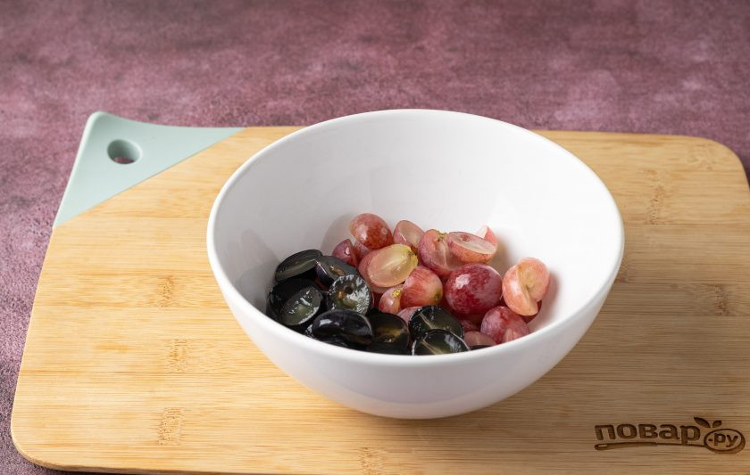 1. Этап. Фруктовый салат с клубникой и виноградом: Виноград помойте, отделите ягоды от веточек. Разрежьте каждую ягоду винограда пополам, по желанию удалите косточки. Переложите в миску.