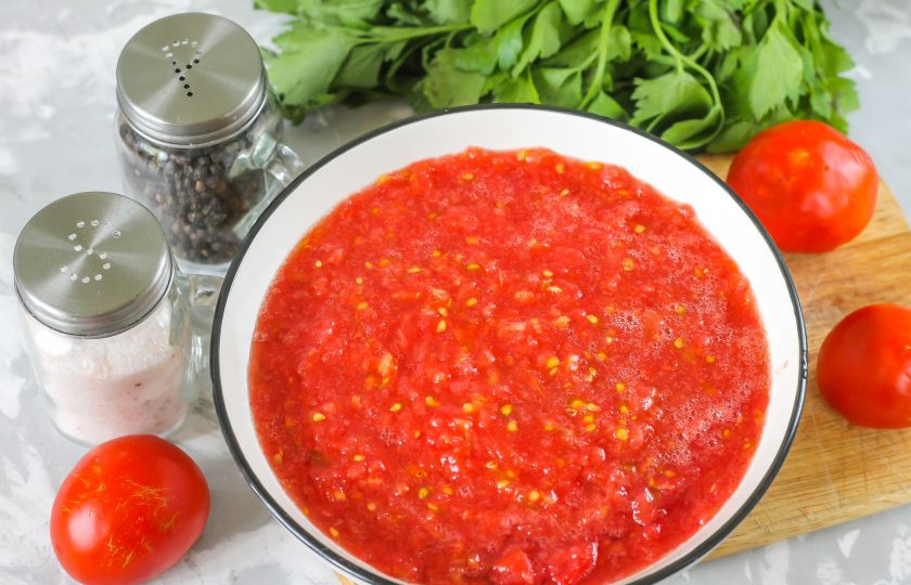 1. Этап. Приправа из помидоров на зиму: Помидоры промойте в воде, разрежьте пополам и удалите зеленые черенки. Протрите каждую половинку томатов на терке с крупными или мелкими ячейками в глубокую миску или салатник.