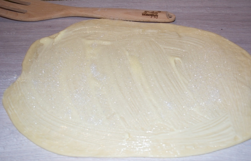 1. Этап. Плюшки с сахаром из дрожжевого теста: Сливочное масло растопите в микроволновке до состояния мягкости. При помощи кисточки смажьте корж теста маслом с одной стороны.