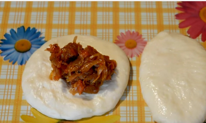 1. Этап. Жареные пирожки с капустой на кислом молоке: 6. Смажьте руки подсолнечным маслом. Выдавите из теста шарики, пальцами придайте им плоскую форму, в центр выкладывайте начинку. Аккуратно закройте края, формирую пирожок.