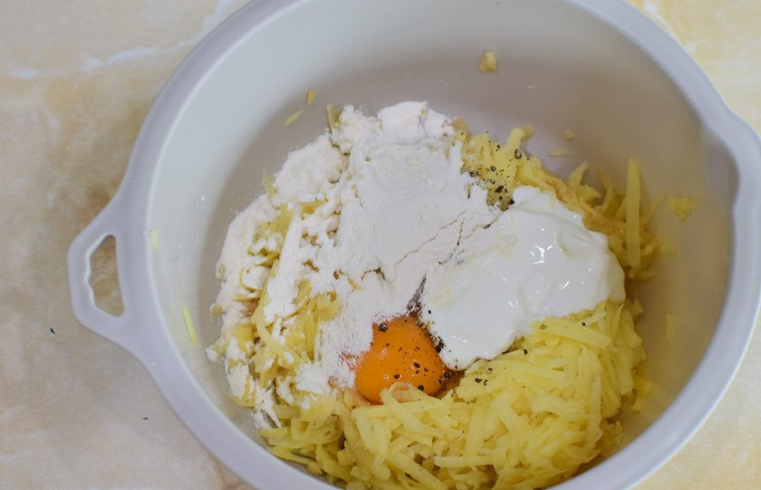 1. Этап. Свиные отбивные в картофельном кляре на сковороде: Для кляра потрите картофель на крупной терке. Слейте с него жидкость. Добавьте к картофелю яйцо, сметану и муку. По вкусу посыпьте солью и специями. Все ингредиенты смешайте.