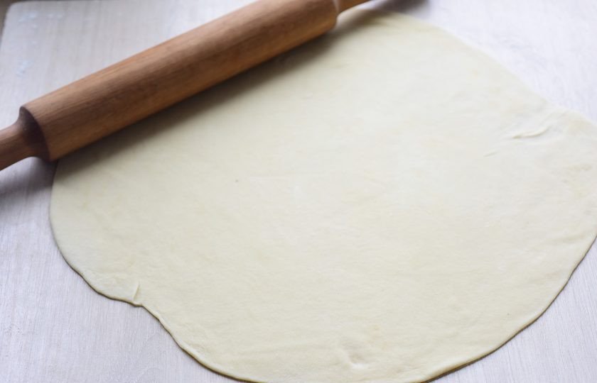 1. Этап. Слоеные лепешки с луком на сковороде: Рабочую поверхность припылите мукой. Раскатайте половину теста в тонкий пласт.