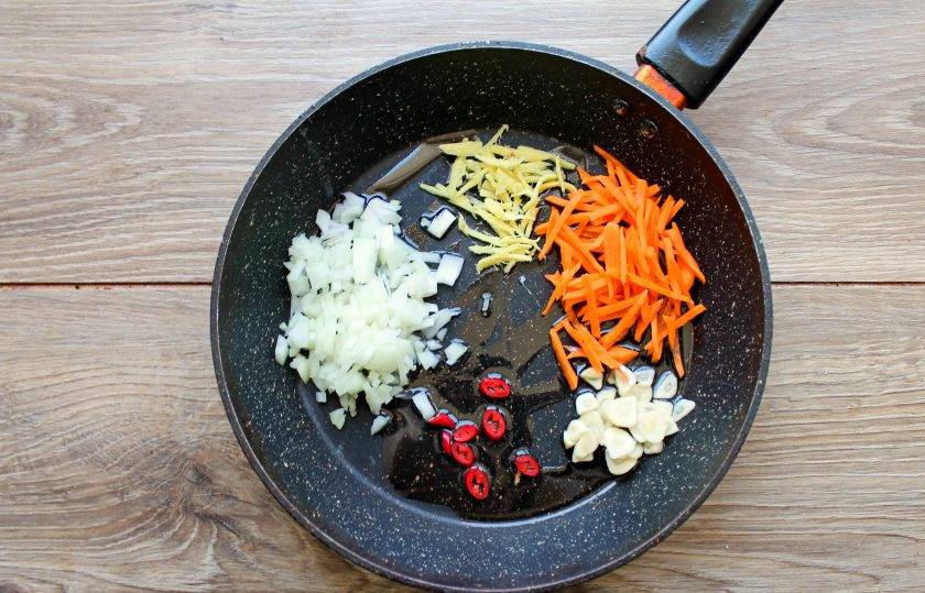 1. Этап. Кальмары по-азиатски: В сковороду налейте растительное масло и добавьте порезанные тонкой соломкой имбирь и морковь. Добавьте мелко нарезанный репчатый лук, чеснок и чили порезанные колечками. Обжаривайте все на среднем огне, перемешивая, в течение 2-3 минут.