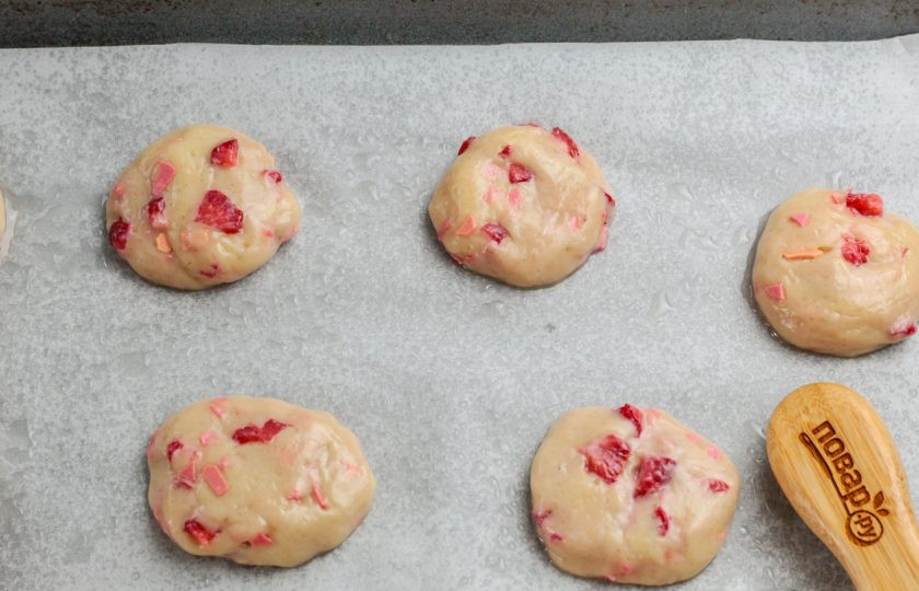 1. Этап. Печенье с клубникой и шоколадом: Разделите тесто на части. Застелите противень пергаментной бумагой и скатайте части теста в руках в колобки. Выложите их на пергаментную бумагу. По желанию можно сбрызнуть ее растительным маслом.