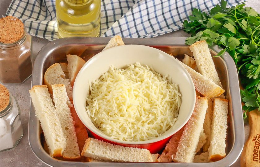 1. Этап. Запеченный Сулугуни: Попробуйте сыр на вкус перед началом приготовления блюда. Если он соленый, то исключите соль из списка ингредиентов. Натрите Сулугуни на терке с мелкими ячейками и выложите в огнеупорную фаянсовую или стеклянную форму. Целой шайбой сыр не запекайте, потому что он расплавляется и совершенно не держит форму. Сыр нужно запекать только в горшочке или в форме. Нарежьте ломтики хлеба пополам или брусочками, как сухарики. Выложите в форму.