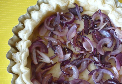 1. Этап. Слоеный пирог с беконом и ветчиной: Красный лук нарежьте полукольцами и обжарьте его на сковороде, добавив растительное масло. Достаньте пирог из духовки и выньте пергамент с фасолью. На дно пирога выложите жаренный лук.