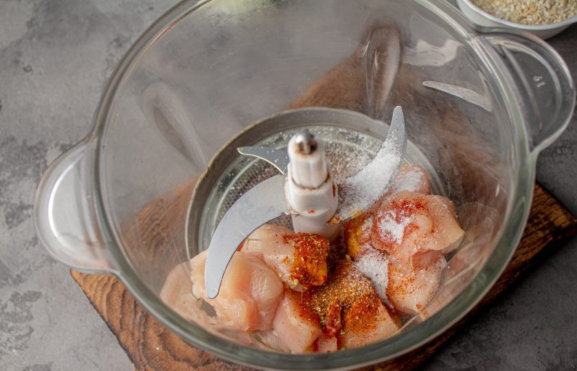 1. Этап. Наггетсы в духовке без масла: Куриное филе нарежьте на кусочки, выложите в чашу измельчителя, добавьте специи.