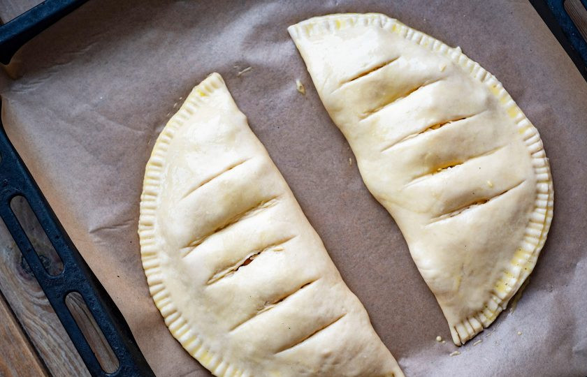 1. Этап. Кальцоне с ветчиной: На противень застеленный пергаментом для выпекания выложите две заготовки кальцоне с ветчиной, на каждой сделайте несколько надрезов для выхода пара, смажьте поверхность взболтанным яйцом и отправьте в уже разогретую до 180 градусов духовку на 20-25 минут.