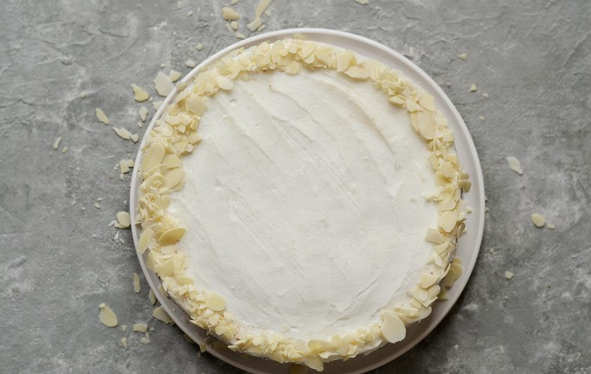 1. Этап. Торт из кокосовой муки: Снимите кольцо, разровняйте верхнюю часть крема, остатками смажьте бока. Украсьте торт миндальными лепестками.