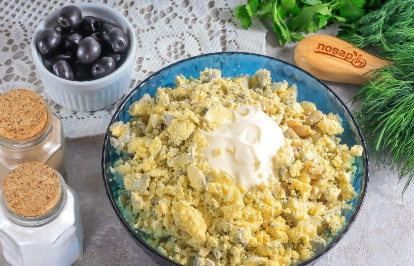 1. Этап. Салат с ананасами на Новый год Кролика 2023: Очистите отварные куриные яйца от скорлупы, промойте в воде и разделите на желтки и белки. 1 яйцо и 1 желток оставьте целым, они понадобятся для пяточек и хвостика кролика. Желтки раскрошите в емкость к нарезкам. Выложите майонез любой жирности, посолите и поперчите. Аккуратно перемешайте салат.