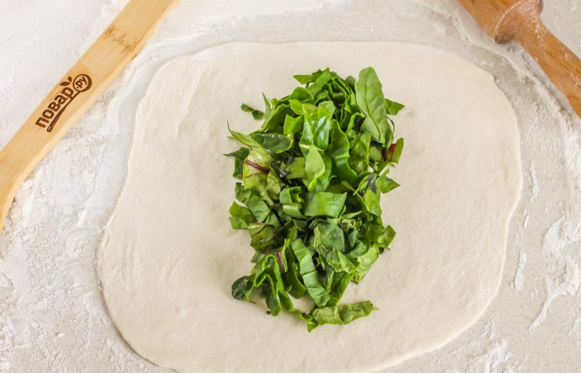 1. Этап. Жингялов хац: Разделите тесто на несколько частей, каждую из них скатайте колобком. Каждый колобок раскатайте в тонкий округлый пласт. Выложите на его середину часть зелени.
