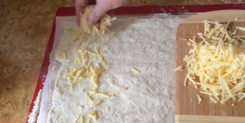 1. Этап. Чамбелла на закваске: 3. Накройте крышкой и оставьте на три часа при комнатной температуре. Выложите тесто на пергамент, присыпанный мукой. Аккуратно сформируйте руками прямоугольник, равномерно посыпьте тертым сыром и мелко нарезанной зеленью.