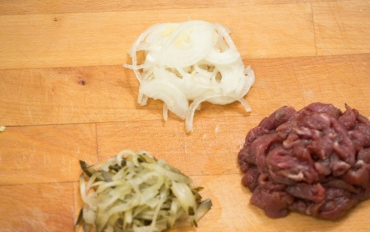 1. Этап. Азу по-татарски из говядины: 2. Первым делом вымойте и обсушите мясо, нарежьте его тонкими полосочками. Нарежьте очищенный лук и соленый огурец.