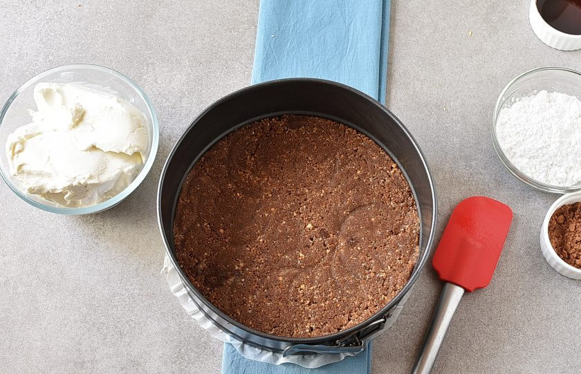 1. Этап. Шоколадный Чизкейк: Застелите дно разъемной формы пергаментом для выпечки. Выложите смесь печенья и хорошо утрамбуйте ее. Уберите в холодильник на 15 минут.