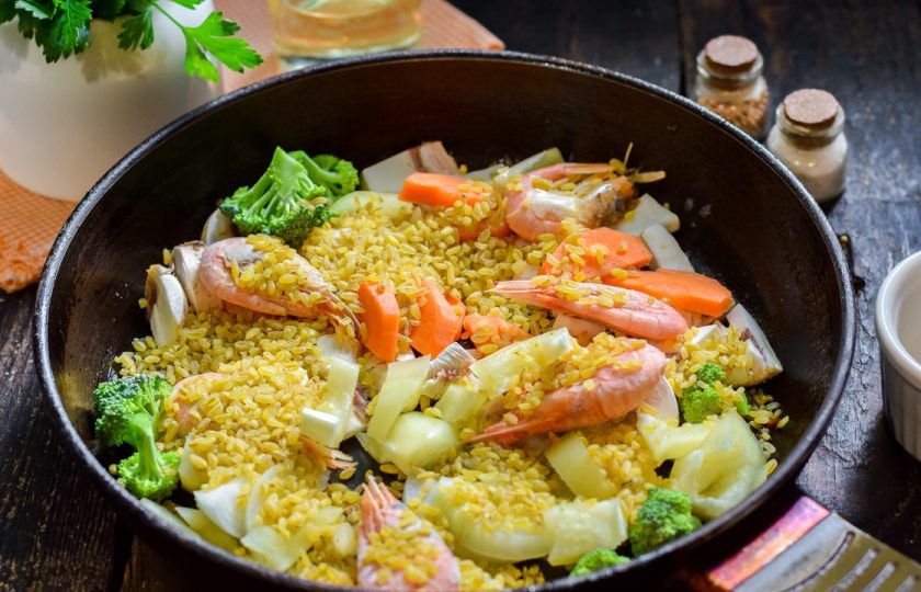 1. Этап. Булгур с овощами и креветками: Всыпьте в сковороду булгур. Добавьте соль и перец по своему вкусу.