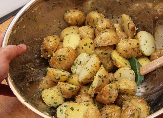 1. Этап. Картофельные дольки в специях: 2. Слейте воду, а картофель остудите немного. Затем нарежьте каждую картофелину пополам, выложите в глубокую мисочку. Добавьте примерно половину от общего количества орегано, петрушки и измельченного чеснока. Посолите по вкусу, сбрызните оливковым маслом. Перемешайте как следует. Лучше всего делать это небольшими порциями, чтобы картофель как следует соединился со специями и маслом.