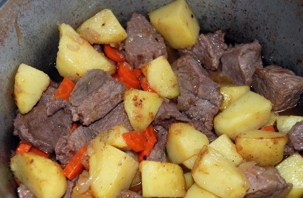 1. Этап. Жаркое по-домашнему из говядины: Выкладываем картофель в казан к остальным ингредиентам, вливаем в него столько воды или бульона, чтобы жидкость доходила почти до картофеля, солим все и перчим. Накрываем казан крышкой, ставим на нее небольшой груз и тушим жаркое на медленном огне 45-50 минут. За минут 15 до готовности вкидываем в казан лавровый лист, всыпаем хмели-сунели и красный перец, перемешиваем все. По прошествии времени выключаем огонь и даем блюду 10-15 минут настояться.
