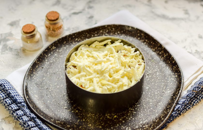 1. Этап. Салат Зимняя ночь: Твердый или адыгейский сыр натрите на средней терке и выложите поверх рыбы.