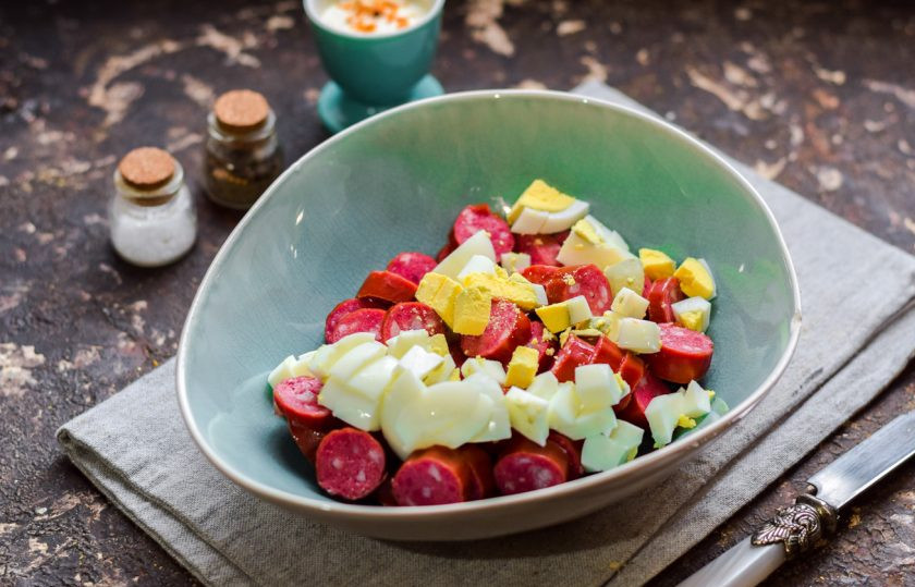 1. Этап. Салат Ежик с колбасой: Куриное яйцо отварите 10 минут, почистите, нарежьте небольшими кубиками. Добавьте яйца в салат.