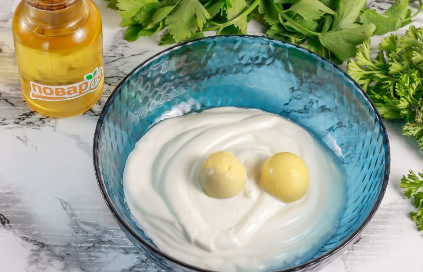 1. Этап. Майонез из сметаны с желтками: Сметану любой жирности выложите в глубокую емкость. Очистите отварные куриные яйца от скорлупы, промойте в воде и разделите на желтки и белки. Желтки добавьте в сметану.