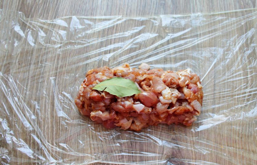 1. Этап. Сальчичон из курицы: Расстелите плотную пищевую пленку и плотно выложите куриный фарш. Выложите сверху лавровый листик.