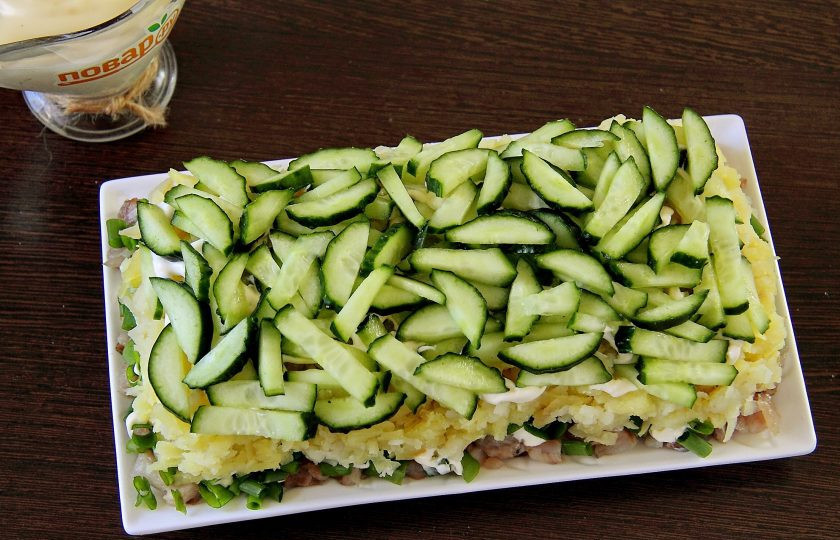 1. Этап. Салат Зеленая шуба: Следующим слоем выкладываем нарезанный огурец и смазываем его майонезом.